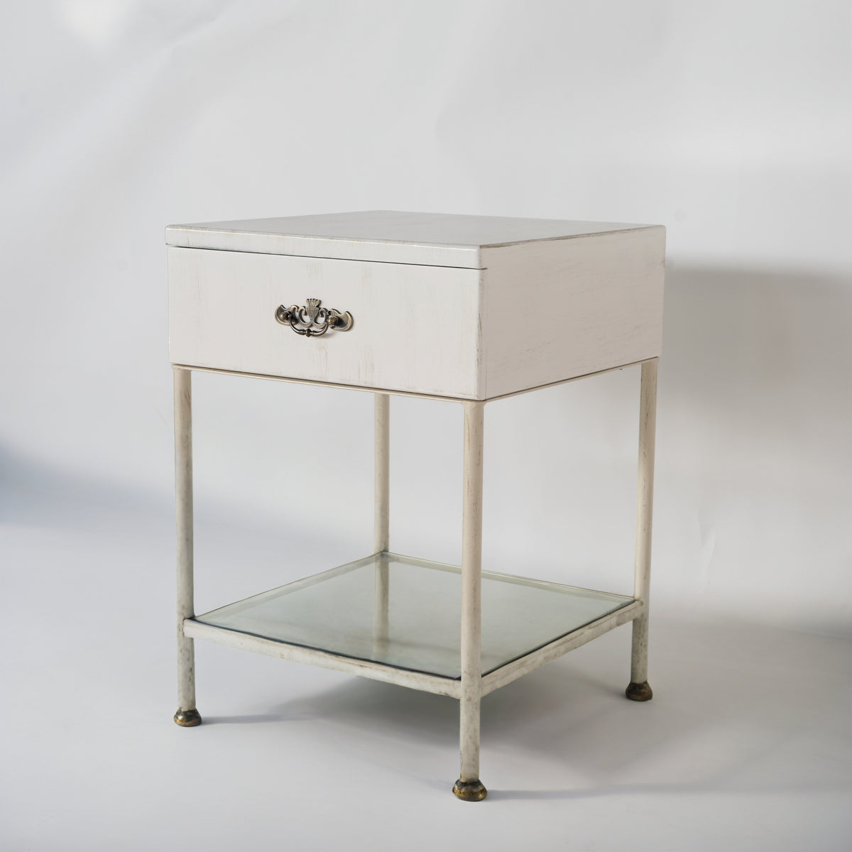 Damme bedside table in white, angled front view with drawer, lower glass shelf and brass feet