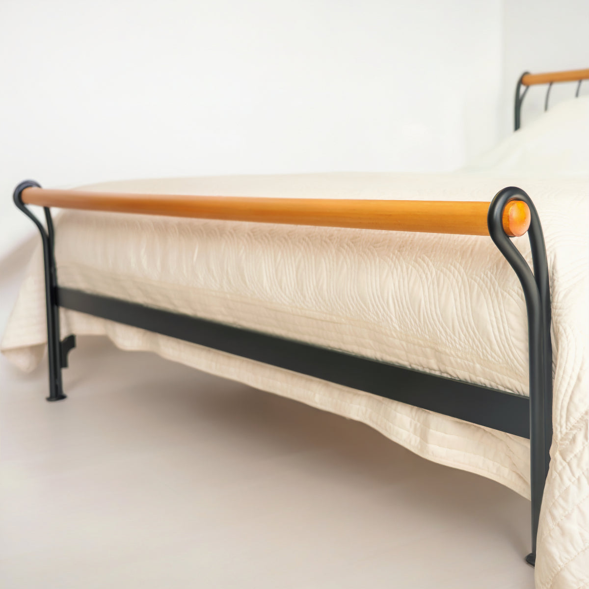 Pied du lit Tivoli avec rail en bois et cadre noir, vu de biais avec la tête de lit à l'arrière
