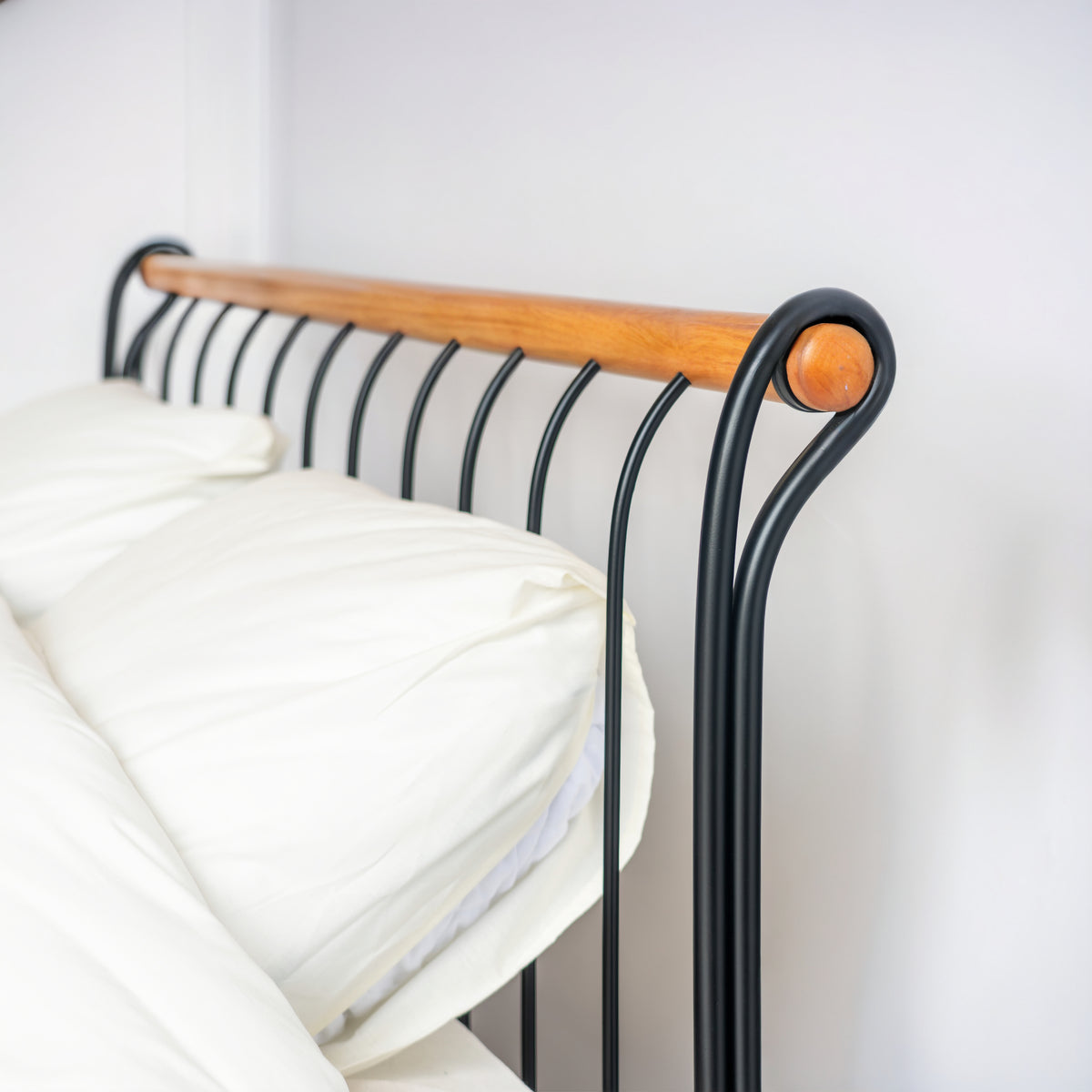 Vue de côté de la tête du lit Tivoli à barreaux noirs, rail en bois et volute en métal à l'extrémité