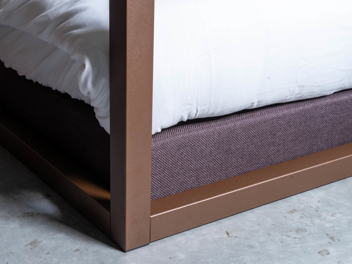 Corner leg of The Loft canopy bed with headboard in metallic brown, with a purple-grey upholstered base