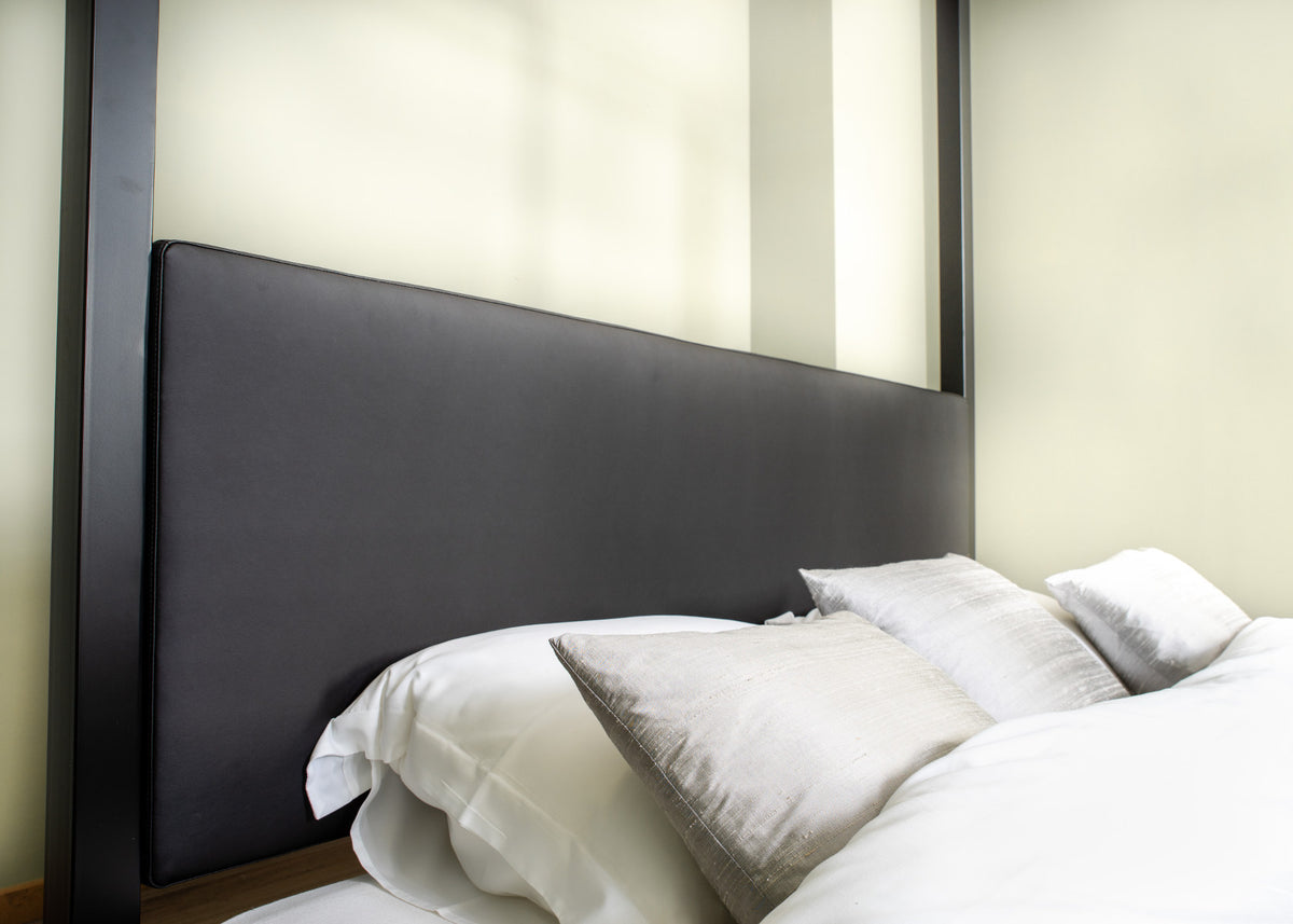 Black upholstered head end of The Loft canopy bed with headboard between the posts, with white pillows