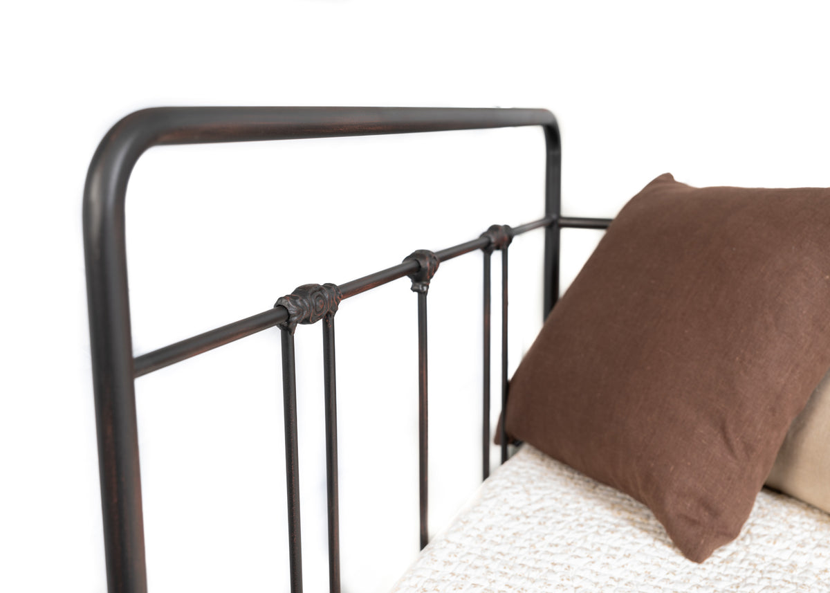 Corner of the Veurne metal single bed with rounded top rail, spindles and decorative joints next to a pillow