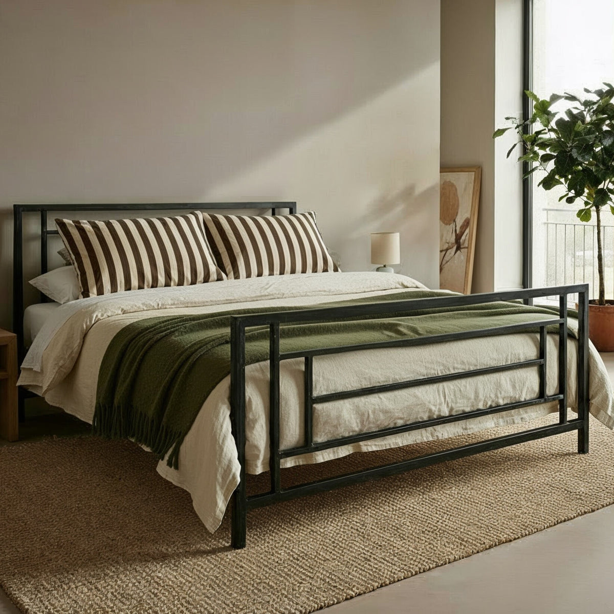 Metallbett Hasselt in Schwarz mit gestreiften Kissen und grünem Plaid, schräg von vorn auf einem Juteteppich
