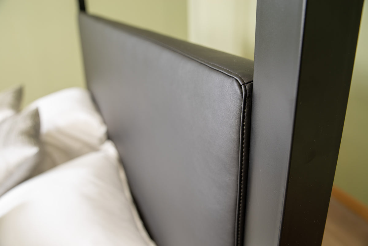 Angled view from above: upholstered head end of The Loft canopy bed with headboard next to a black post